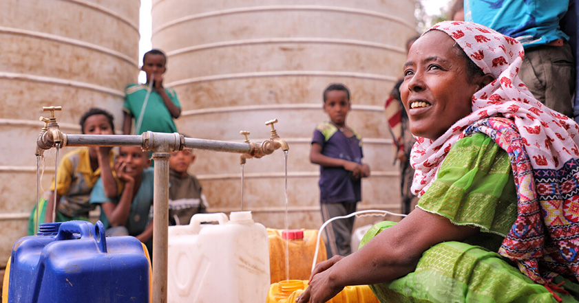 Woman and children next to water tap filling plastic bottles in Tigray, Ethiopia