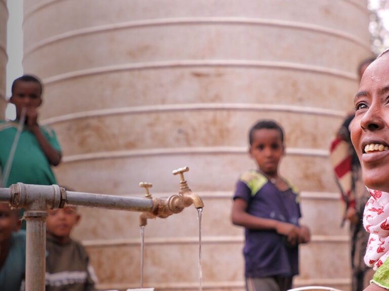 ethiopian woman in pink headscarf sits at water tap with children