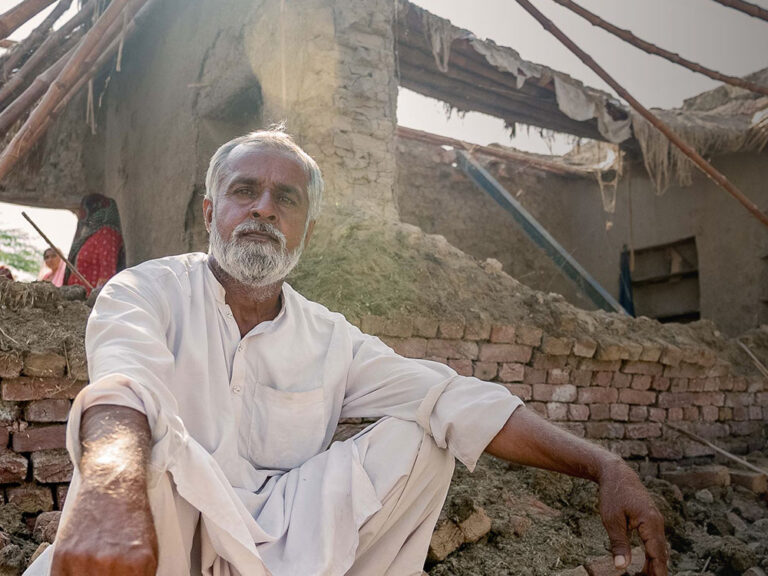 Man in Pakistan crouches outside his home destroyed by flooding