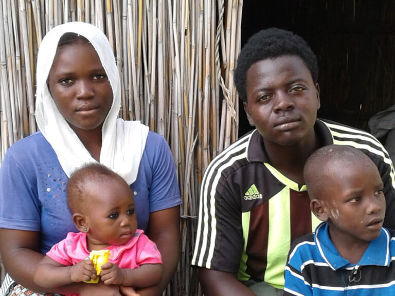 Man, lady and two babies sitting outside a shelter