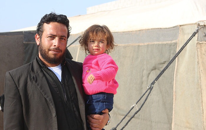 Man holding a child next to a tent in Syria