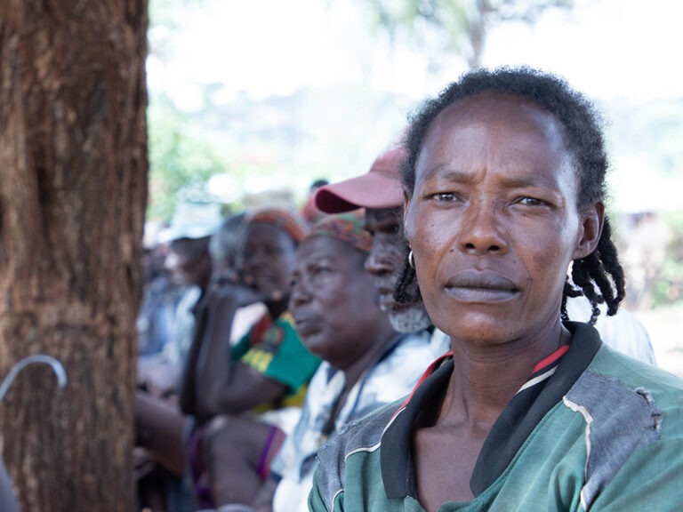 Woman in green sitting on floor outside in Ethiopia, with many others sitting behind her.