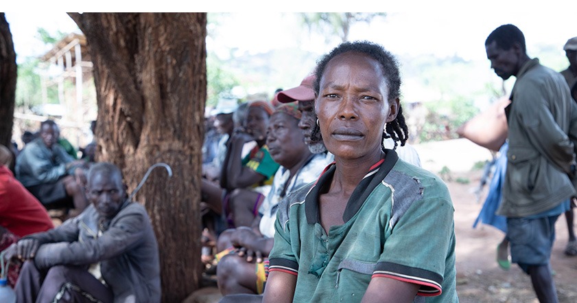 Woman in green sitting on the floor in Ethiopia, with many others sitting on the floor behind her.