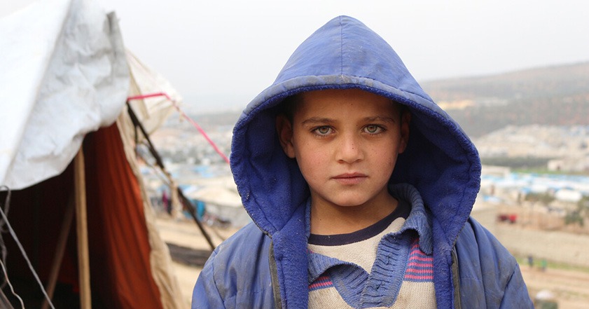 Close up image of a child in a winter coat in front of a tent