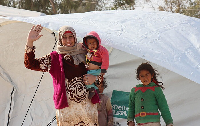 Woman and three children in warm clothes outside a tent in Syria