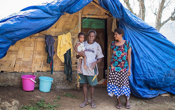 Woman and man holding a child outside a shelter in Vanuatu after their home was destroyed in a storm