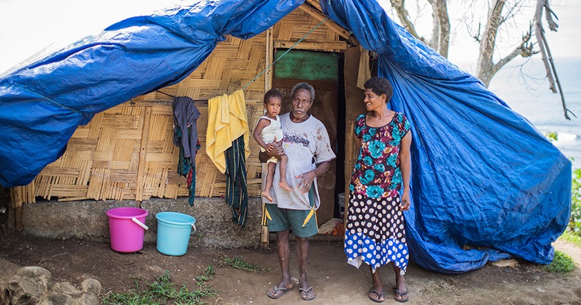 Woman and man holding a child outside a shelter in Vanuatu after their home was destroyed in a storm