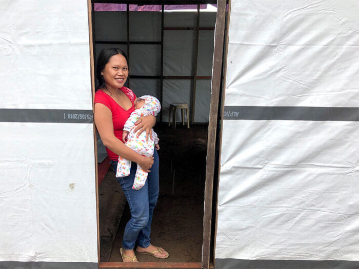 woman in the Philippines standing at her door with her baby