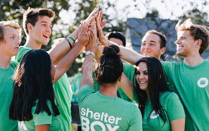 Group of people high fiving while wearing ShelterBox tshirts